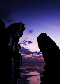 Silhouette rock formation in sea against sky during sunset