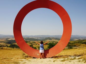 Rear view of woman standing against circular structure on field against clear sky