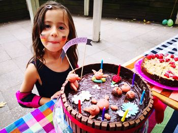 Portrait of smiling girl standing by birthday cake on table