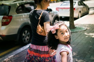 Portrait of smiling girl with mother walking on footpath