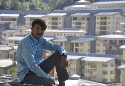 A young guy looking at camera sitting outside with buildings in background with copy space 