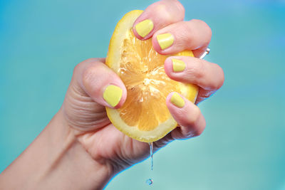 Cropped image of hand squeezing fruit against blue sky