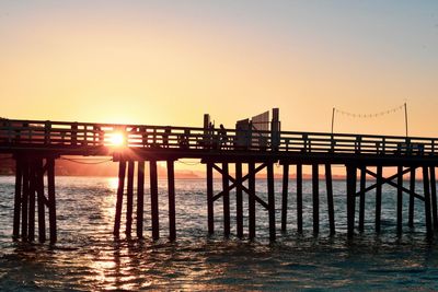 Silhouette pier on sea against clear sky during sunset