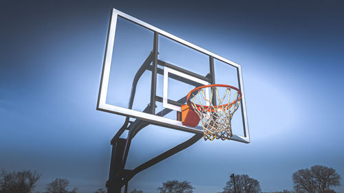 Trees below the basketball hoop with vibrant blue sky background 