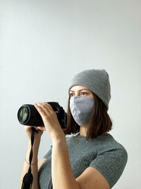 Young female photographer in reusable face mask with camera on a white background. photographing.