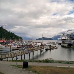 Boats in harbor against cloudy sky