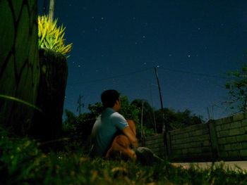 Man sitting in park against sky at night