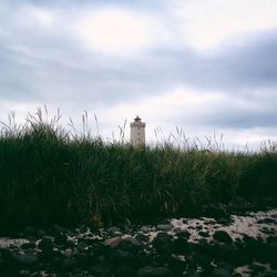 Lighthouse on grassy field against cloudy sky