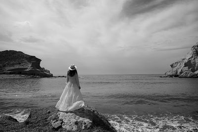 Woman standing on rock by sea against sky