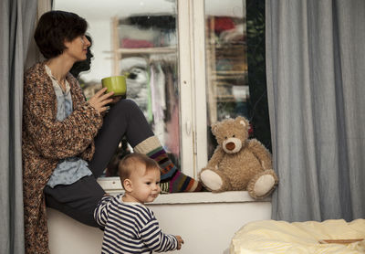 Woman having drink while siting on window