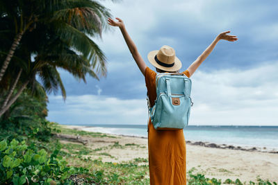Man standing by palm tree on beach against sky