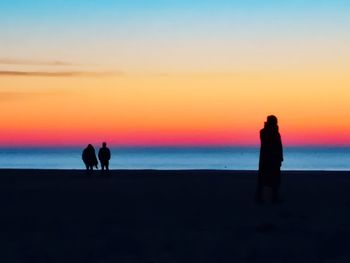 Silhouette people on beach against sky during sunset