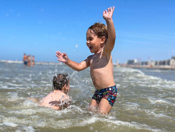 Shirtless man with arms raised standing in sea