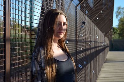 Portrait of beautiful young woman standing against fence