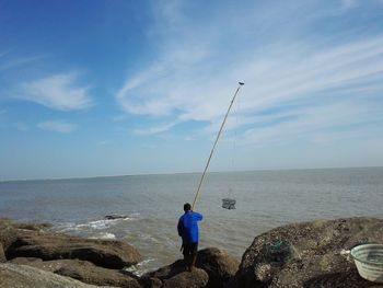 Rear view of man fishing in sea against sky