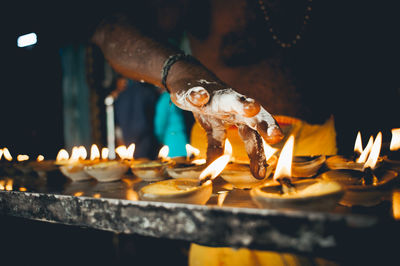 Midsection of shirtless man placing diyas on table in temple