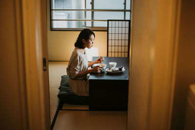 Side view of man using mobile phone while sitting on table