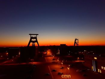 Illuminated factory against sky at sunset