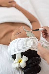 Cropped hands of beautician applying facial mask on woman face at spa