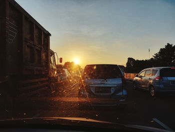 Cars on road against sky during sunset in city