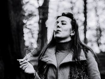 Young woman smoking while standing against trees