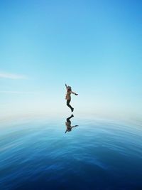 Digital composite image of woman jumping over sea against sky