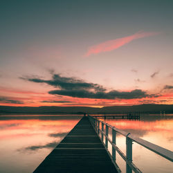 Pier over lake against romantic sky at sunset