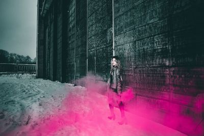 Portrait of woman holding distress flare while standing by building during winter