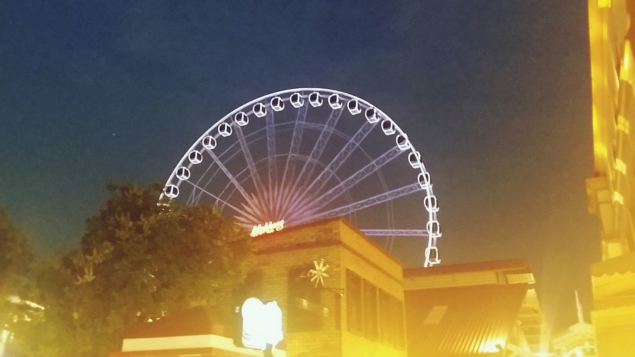 low angle view, amusement park, ferris wheel, arts culture and entertainment, amusement park ride, illuminated, sky, built structure, silhouette, architecture, night, circle, dusk, sunset, outdoors, lighting equipment, fun, tree, no people, incidental people