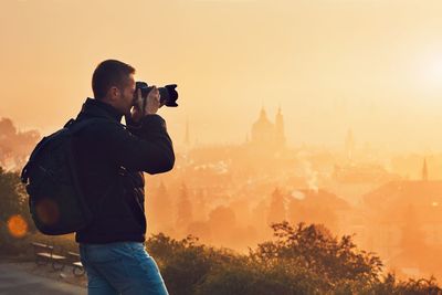 Man photographing cityscape against sky during sunset