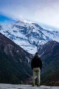 Rear view of man standing against snowcapped mountains