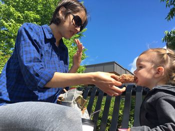 Low angle view of mother feeding daughter while sitting at cafe