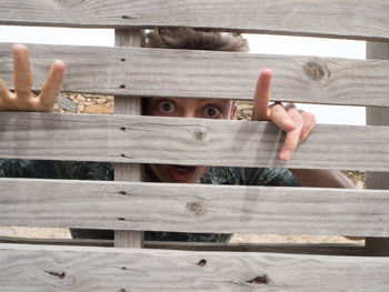 Portrait of young man looking through wooden fence
