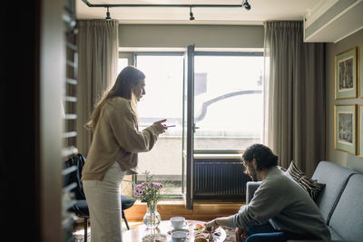 Rear view of man and woman using phone while sitting on table