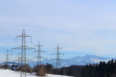 Electricity pylon by trees against sky