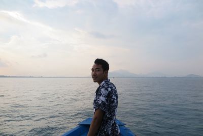 Side view of young man standing in sea against sky