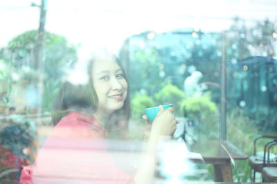 Portrait of smiling woman with coffee in cafe seen through window