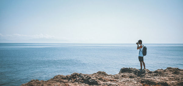 Woman standing on rock by sea against sky