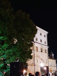 Illuminated tree by building against sky at night