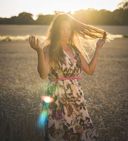 Mid adult woman wearing dress while standing on field at sunset