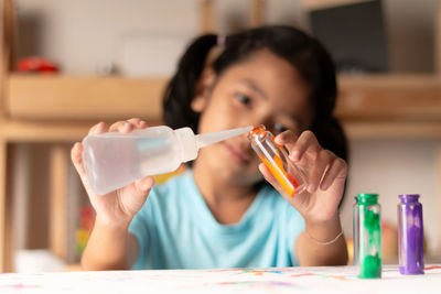 Cute girl pouring water in color bottle on table at home