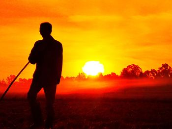 Silhouette man standing on field against orange sky