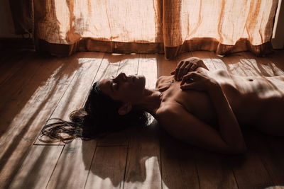 High angle view of topless woman lying on hardwood floor at home