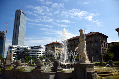 Fountain amidst buildings in city against sky