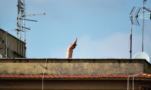 Low angle view of hand against building against clear sky