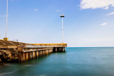 Jetty at calm sea against blue sky