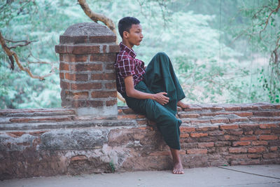 Young man looking away against brick wall