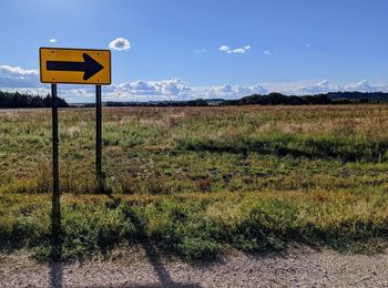 Road sign on field against sky