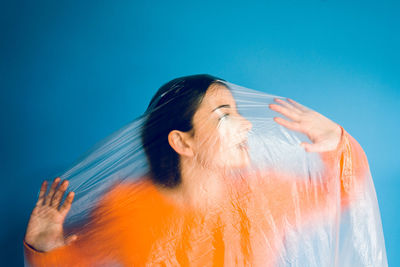 Teenage girl wrapped in plastic against blue background