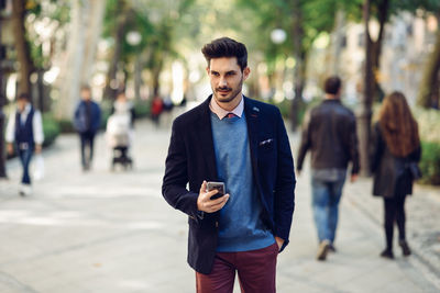 Young man using mobile phone while standing on footpath